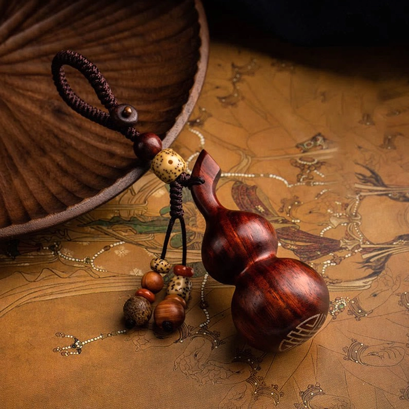 Small leaf red sandalwood vertical gourd keychain flat lay on antique wooden tray, showing natural reddish-brown wood tone and auspicious engraving