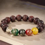 Five Directions Wealth God red sandalwood bracelet with multicolored gemstone beads displayed on vintage book surface