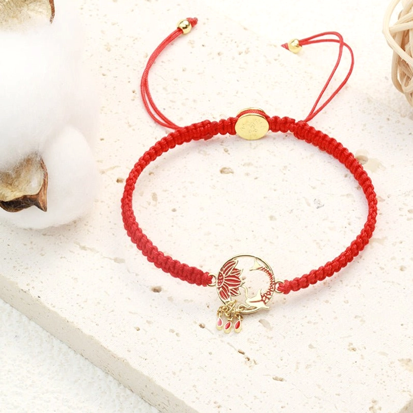 Buddhist red string bracelet with enameled hollow lotus and koi charm, shown with gold fastener and tassel pendant on marble