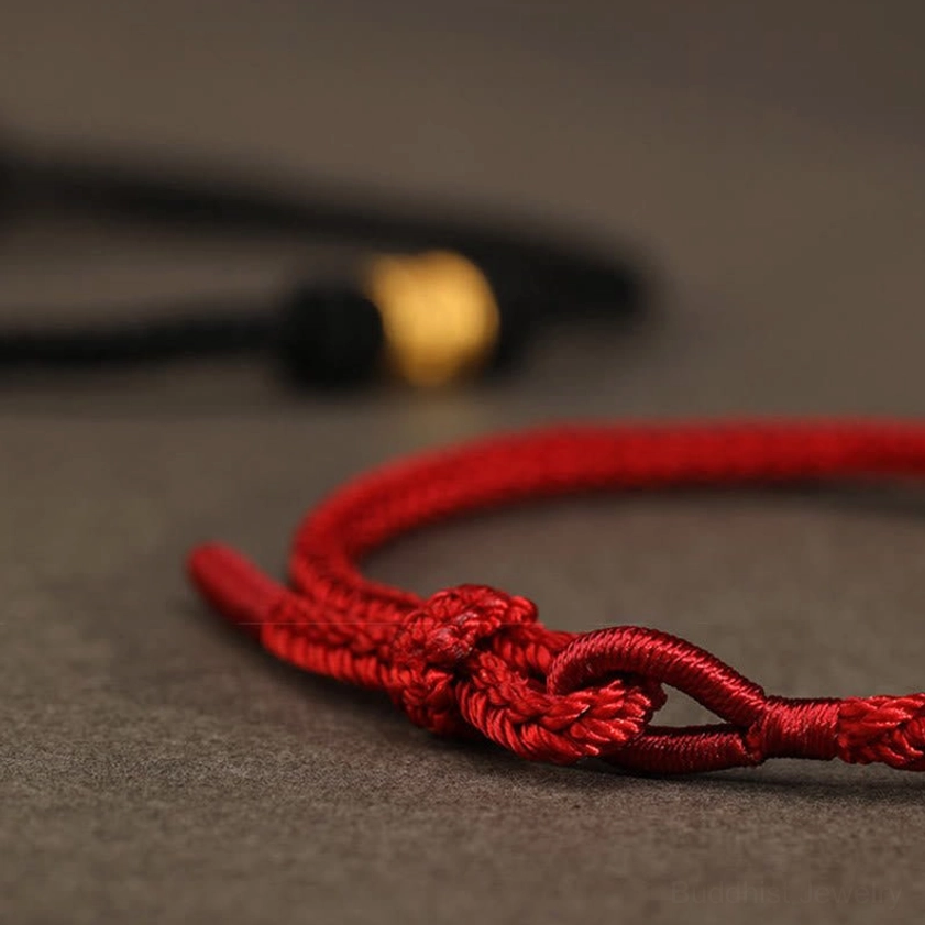Hand-tied red rope knot detail of adjustable Buddhist luck bracelet, intricate craftsmanship