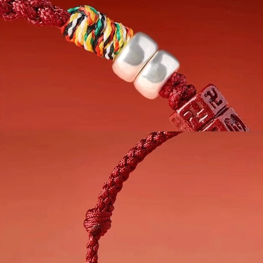 Macro photography of red string bracelet decorations showing woven wraps, silver barrel beads, and engraved cinnabar charm