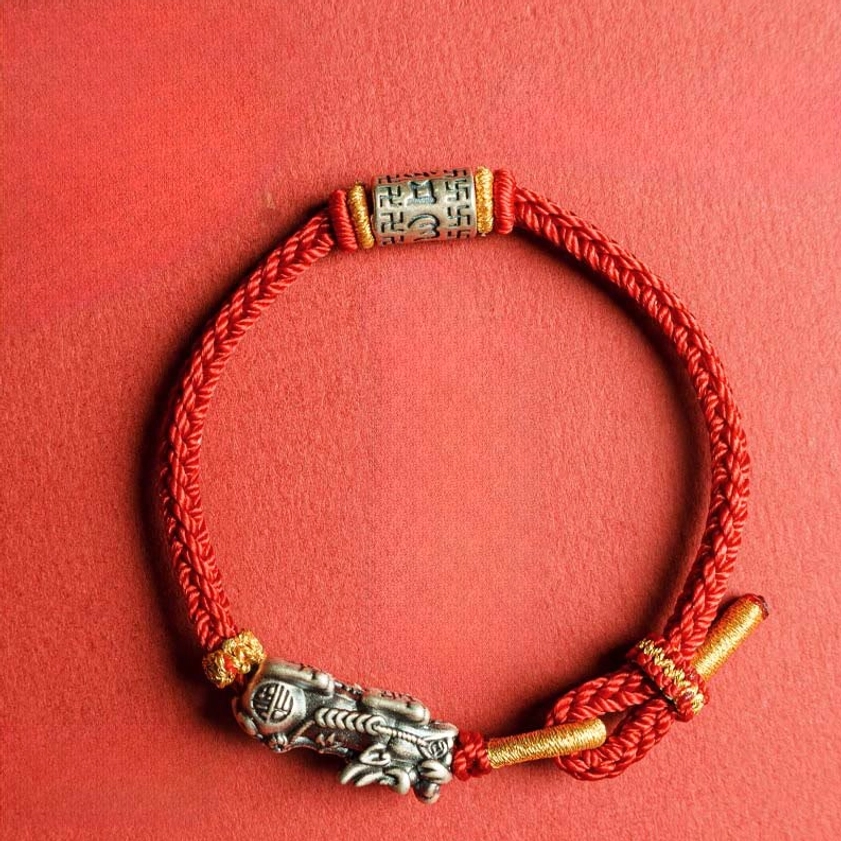 Top-down view of handmade red string bracelet with silver Pixiu charm and Om Mani Padme Hum tube