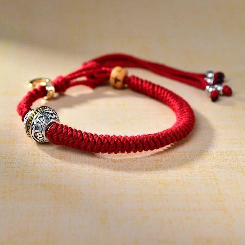 Tibetan red string Buddhist bracelet with carved metal bead and adjustable tassel, three-quarter angle product photo