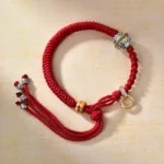 Red string Buddhist diamond knot braided bracelet with copper beads and crystal accents, top view showing intricate weaving pattern