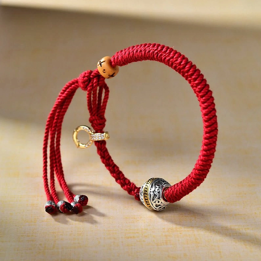 Adjustable red string Buddhist protection bracelet with metal center bead and tassel, three-quarter side view
