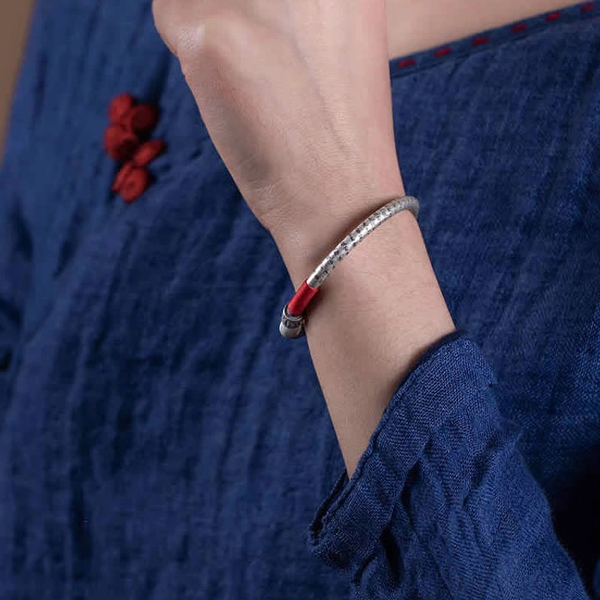 Buddhist red string protection bracelet worn on wrist, side close-up view with traditional indigo clothing background