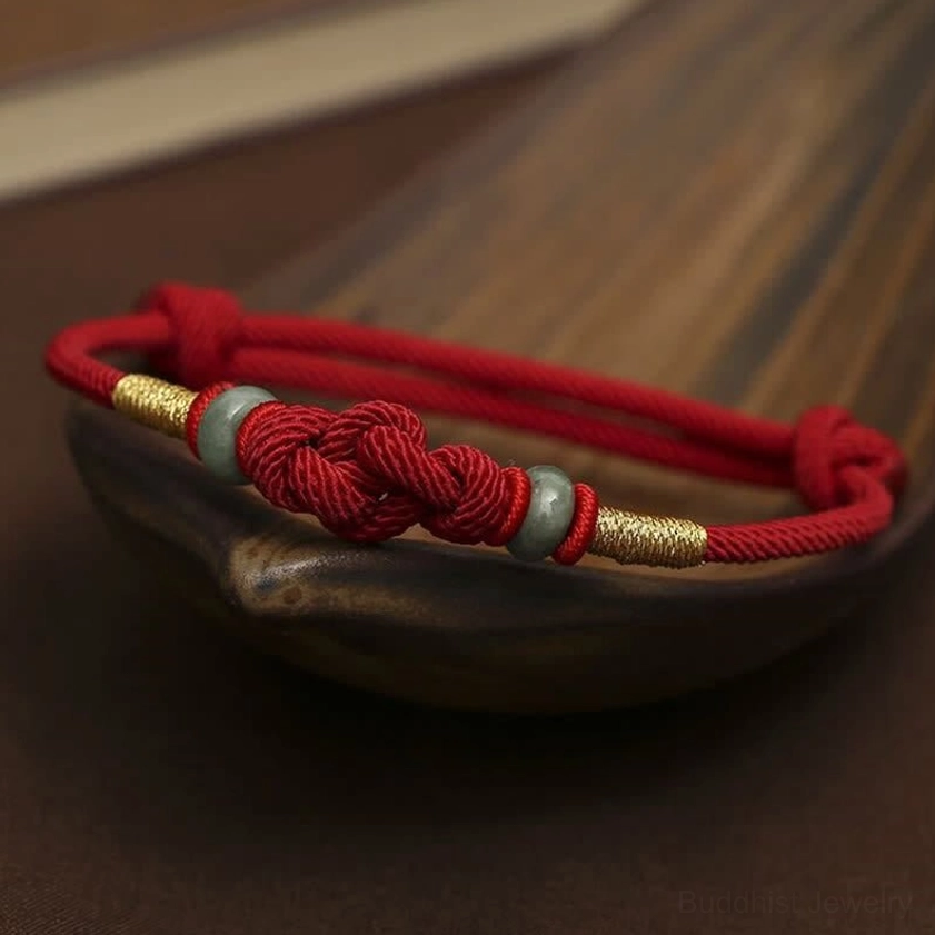 Red jade luck bracelet displayed on dark wooden tray with braided cord and decorative knot