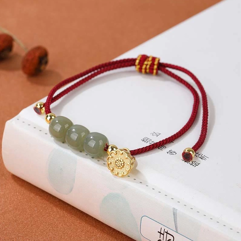 Buddhist red string jade bead bracelet placed on traditional Chinese book, featuring dark red cord and gold lotus pod pendant charm with three smooth jade beads