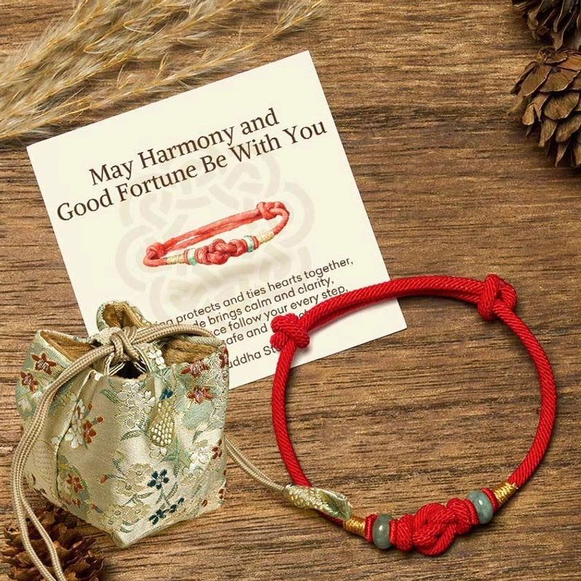 Red string jade Buddhist bracelet with embroidered fabric gift pouch and greeting card on wooden table with pinecones
