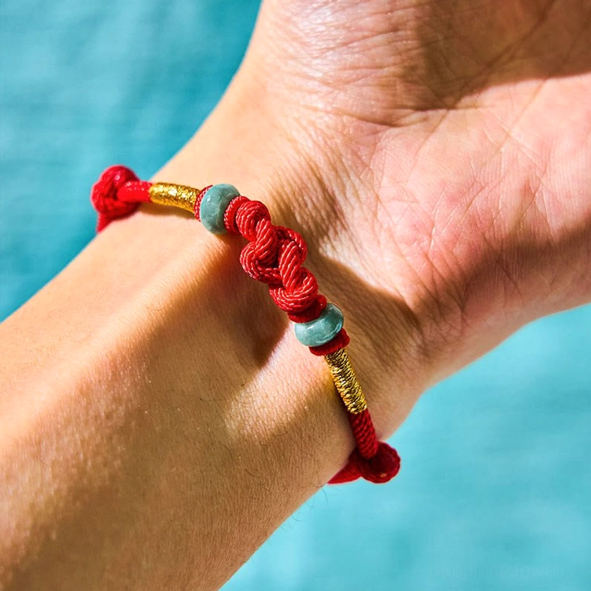 Red string jade bracelet worn on wrist front view with central braided knot
