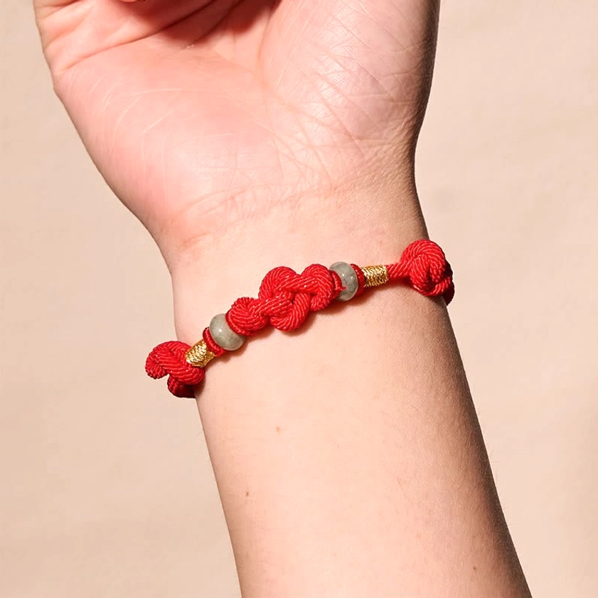 Red string adjustable bracelet worn on wrist with balanced decorative knots and natural jade beads on light background