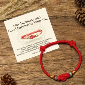 Red string jade Buddhist bracelet with blessing gift card on wooden table with natural pinecones - adjustable protection bracelet