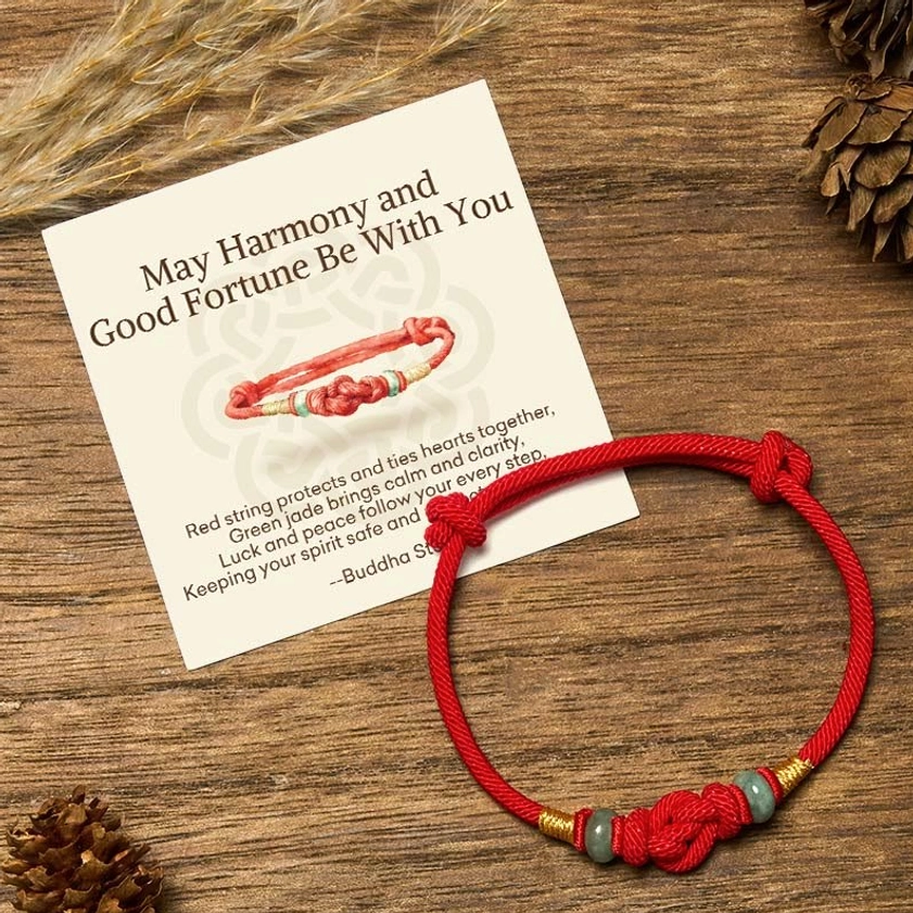 Red string jade Buddhist bracelet with blessing gift card on wooden table with natural pinecones - adjustable protection bracelet