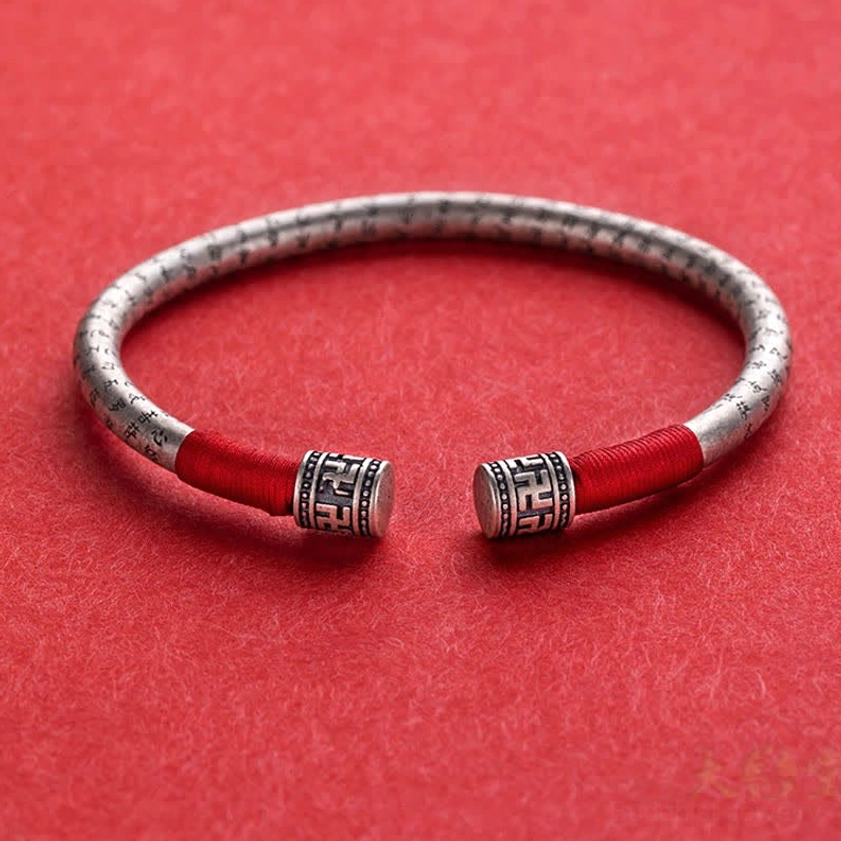 Buddhist luck red string bracelet with dual red wraps and patterned metal ends, overhead flat lay on red fabric