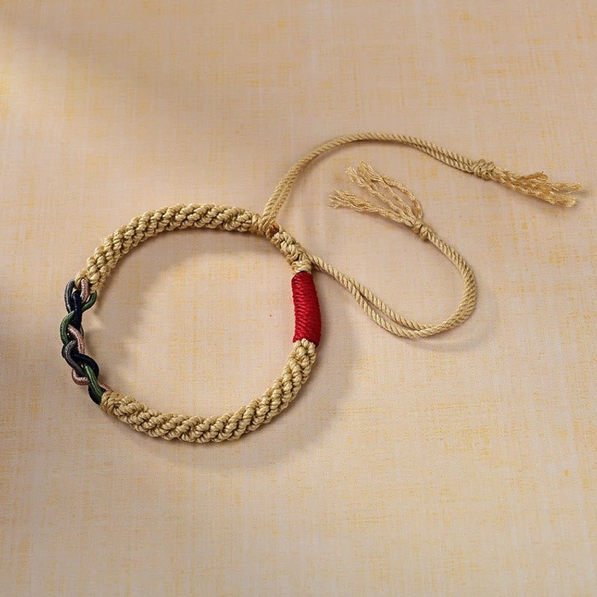 Flat lay overhead view of adjustable Buddhist string bracelet showing natural cotton rope, red accent band, and dark knotted details on brown fabric