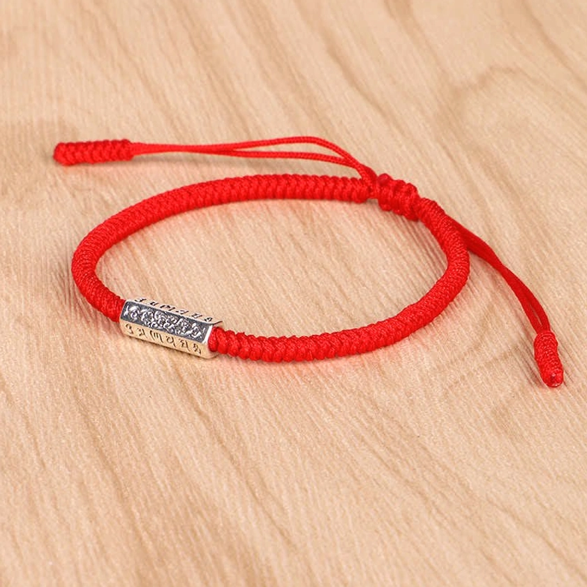 Bright red woven Buddhist bracelet with engraved silver bead and adjustable pull knot design photographed on light wood grain surface