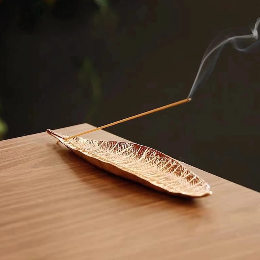 Reddish-brown metal Buddhist leaf incense burner with burning incense and smoke on wooden desk
