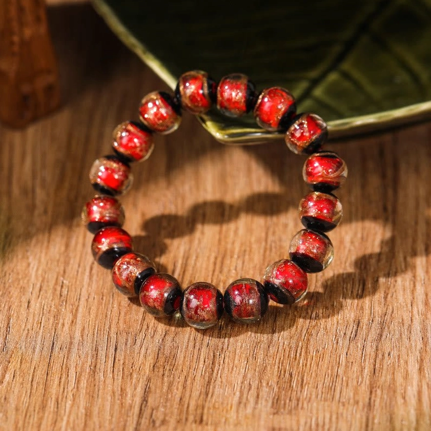 Reddish-brown liuli glass Buddhist bracelet with metallic speckled texture photographed from side on wooden table