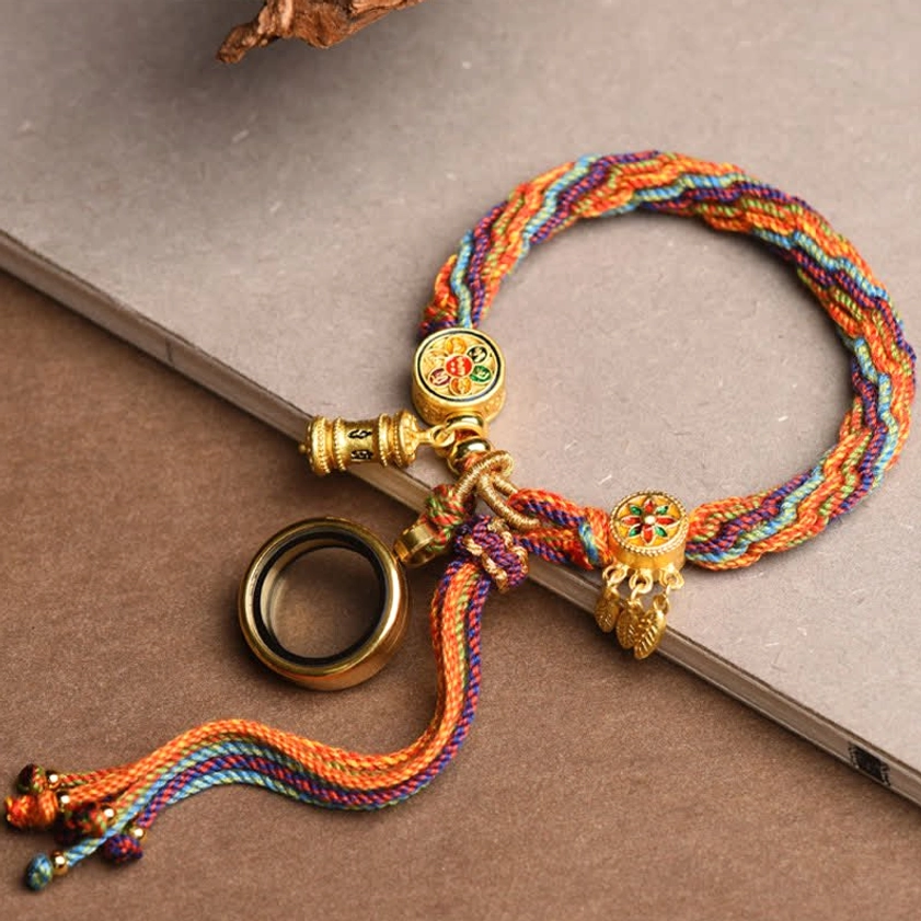 Rainbow braided Buddhist protection bracelet with gold decorative ornaments and lucky knot displayed on book