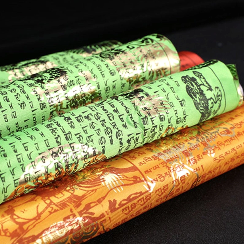 Rolled Buddhist prayer flags with green and orange fabric showing gold foil Tibetan script and traditional patterns close-up