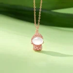 Rose gold chalcedony Buddha pendant necklace with white stone and rhinestone crown detail, worn with green leaf studio background