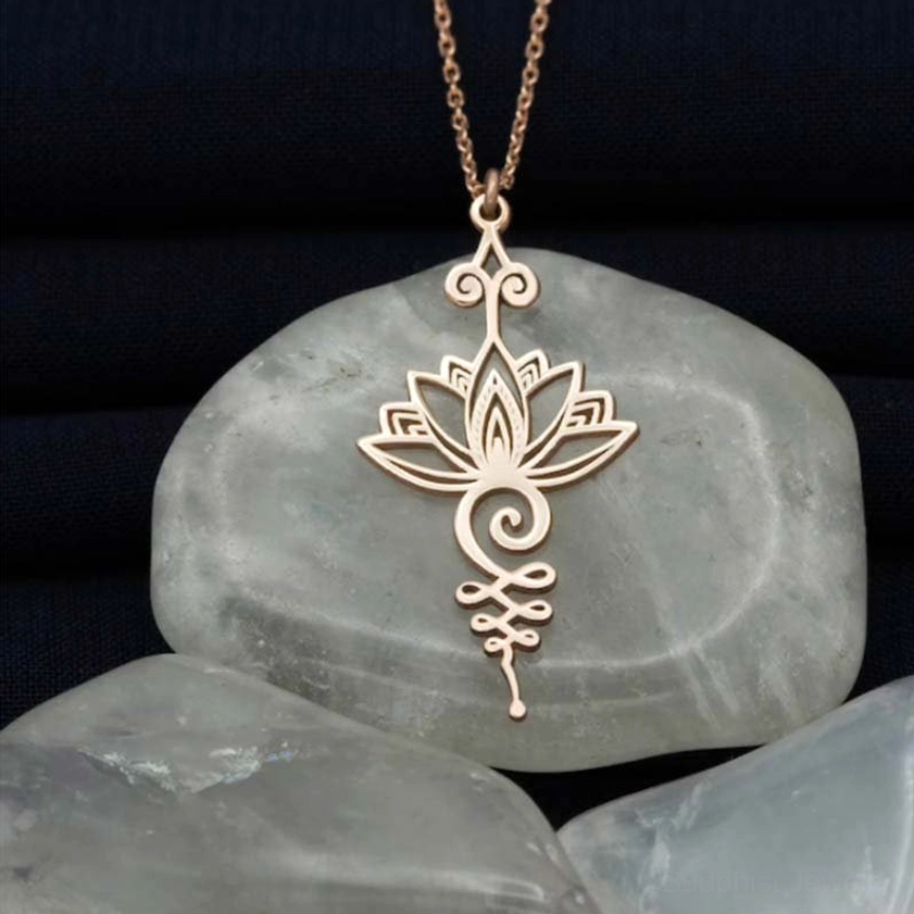Rose gold peachpuff lotus unalome pendant necklace with delicate hollow carved spiritual pattern on dark fabric background