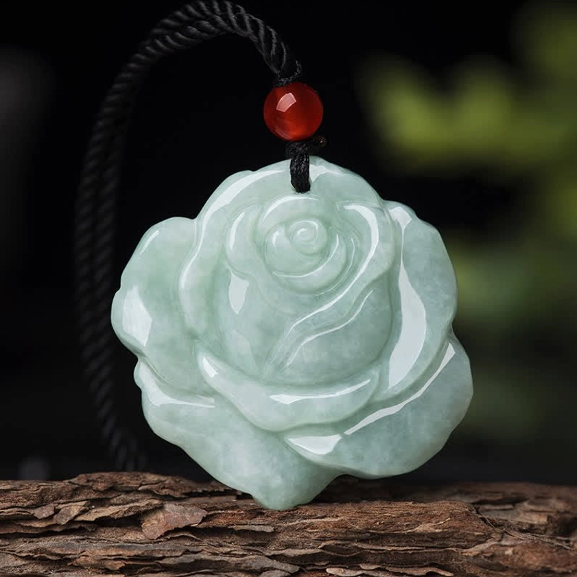 Front close-up of pale green jade rose pendant necklace on wooden bark surface, highlighting three-dimensional carved petal work