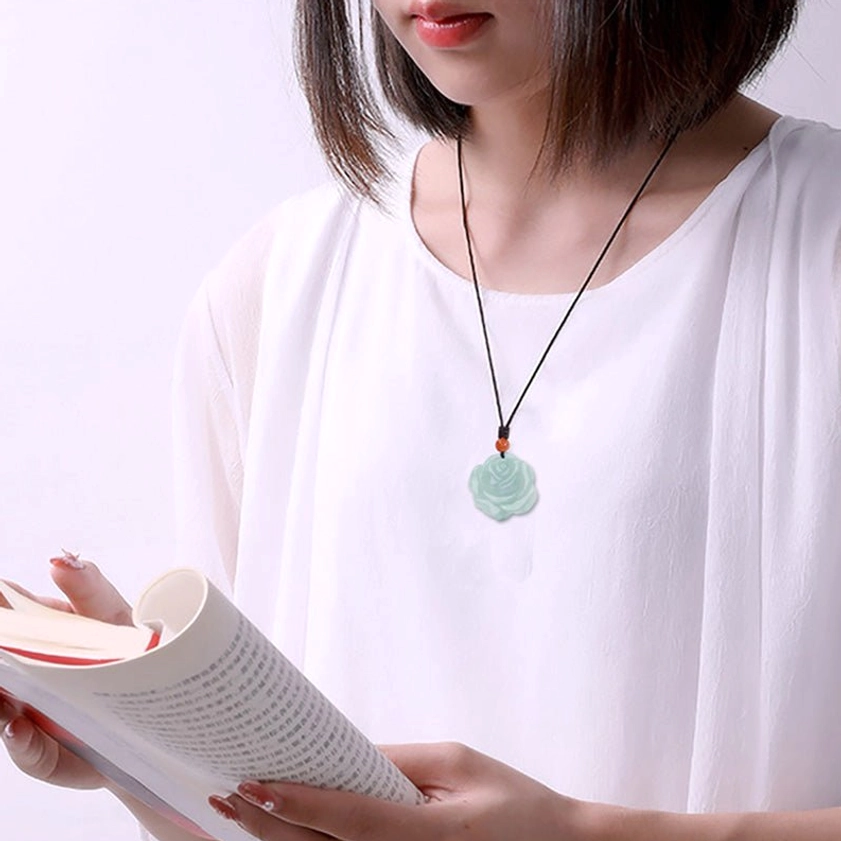Rose jade pendant necklace worn on woman reading indoors, celadon jade carved rose visible, demonstrates everyday spiritual jewelry styling
