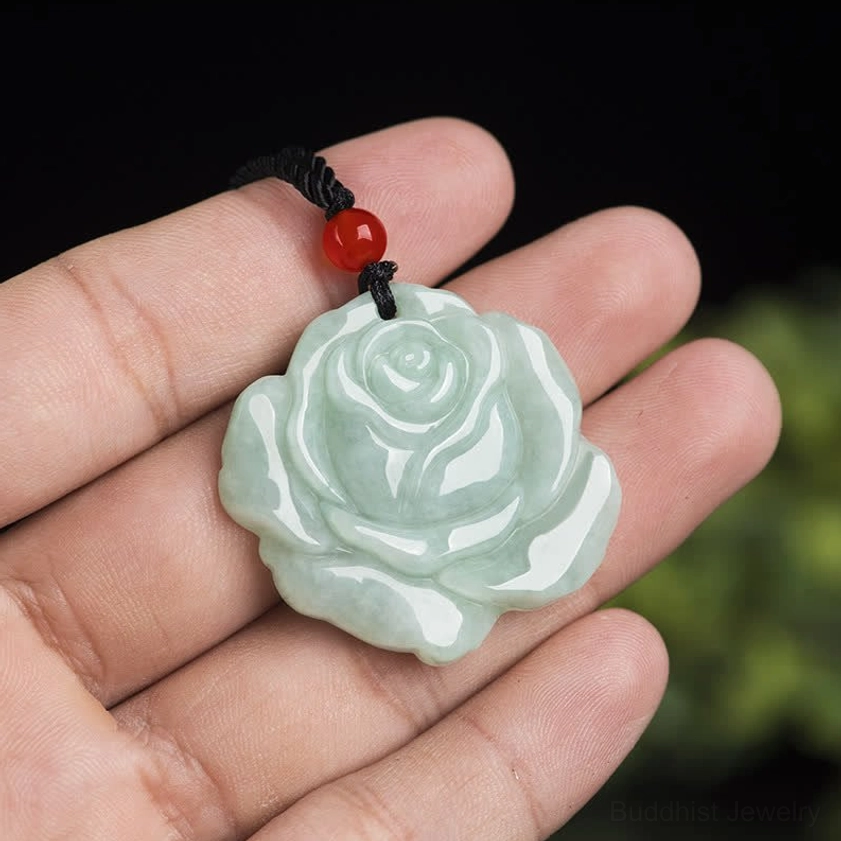 Hand-held rose jade carved pendant with red agate bead displayed on fingertips, light green jade with black cord visible