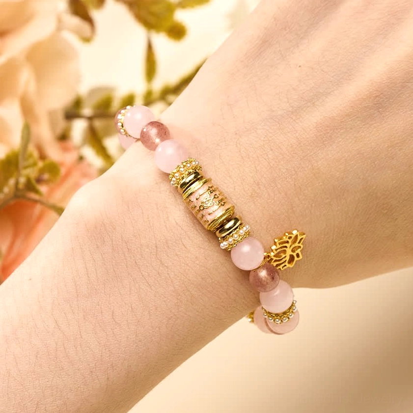 Wrist view of rose quartz healing bracelet with lotus charm worn on human hand with floral background