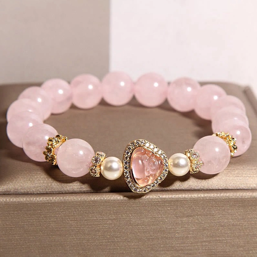 Pink crystal Buddha charm bracelet top-down view on brown jewelry display pad featuring natural rose quartz round beads and gold-toned metal Buddha pendant