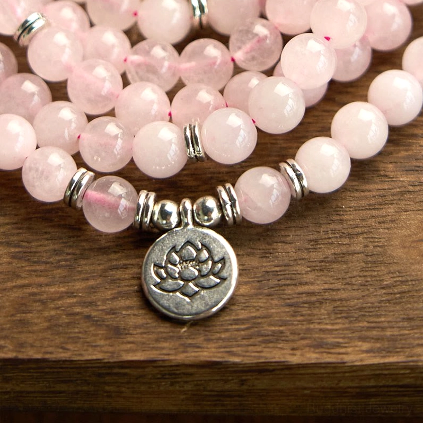 Rose quartz 108 mala beads with large silver lotus pendant charm on wooden surface, overhead view