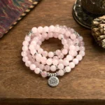 Rose quartz 108 mala beads bracelet with silver lotus pendant charm, overhead flat lay on wooden table