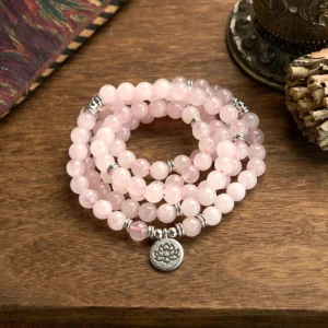 Rose quartz 108 mala beads bracelet with silver lotus pendant charm, overhead flat lay on wooden table