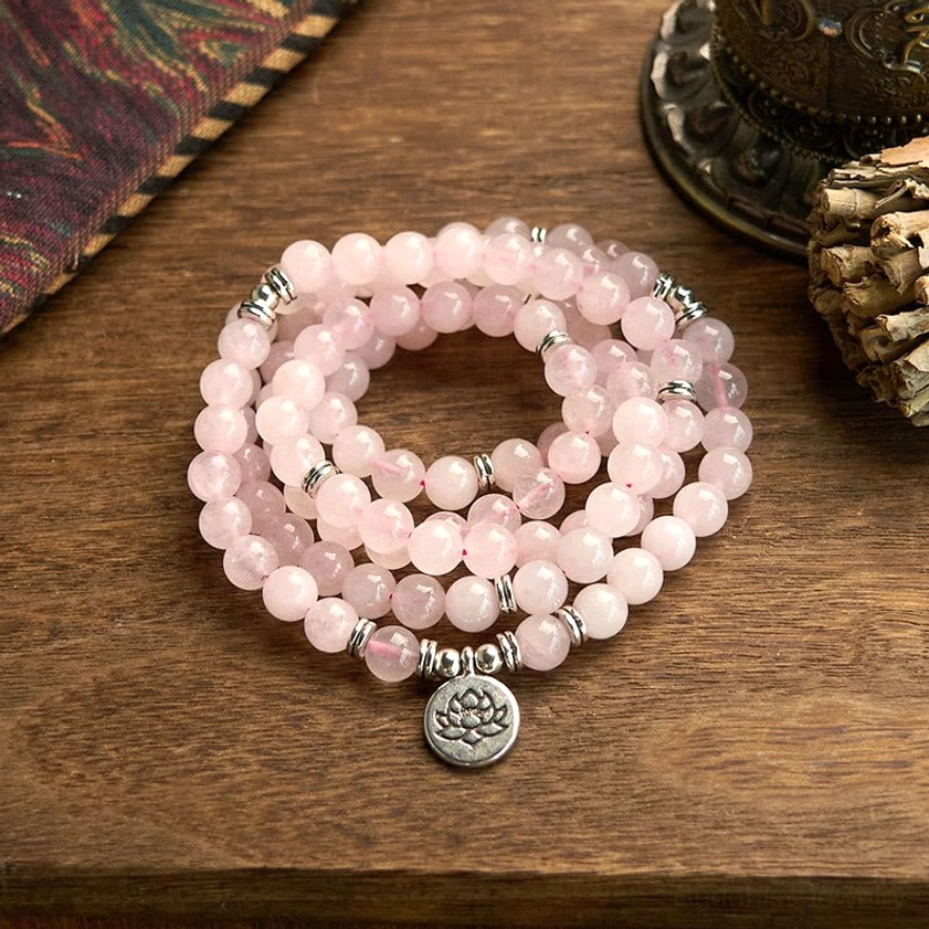Rose quartz 108 mala beads bracelet with silver lotus pendant charm, overhead flat lay on wooden table