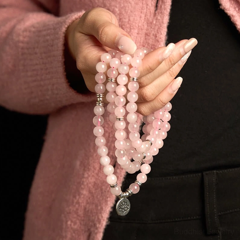 Rose quartz mala beads held in prayer pose hands with silver lotus pendant, close-up meditation