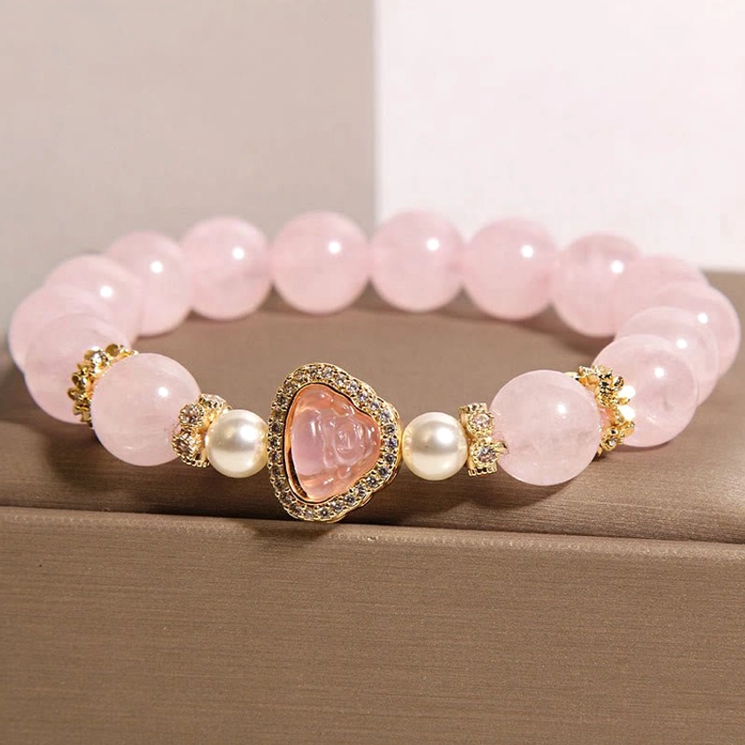 Rose quartz pearl Buddha bracelet high side overhead angle on brown jewelry surface showcasing heart-shaped Buddha pendant with crystal frame and smooth pink beads