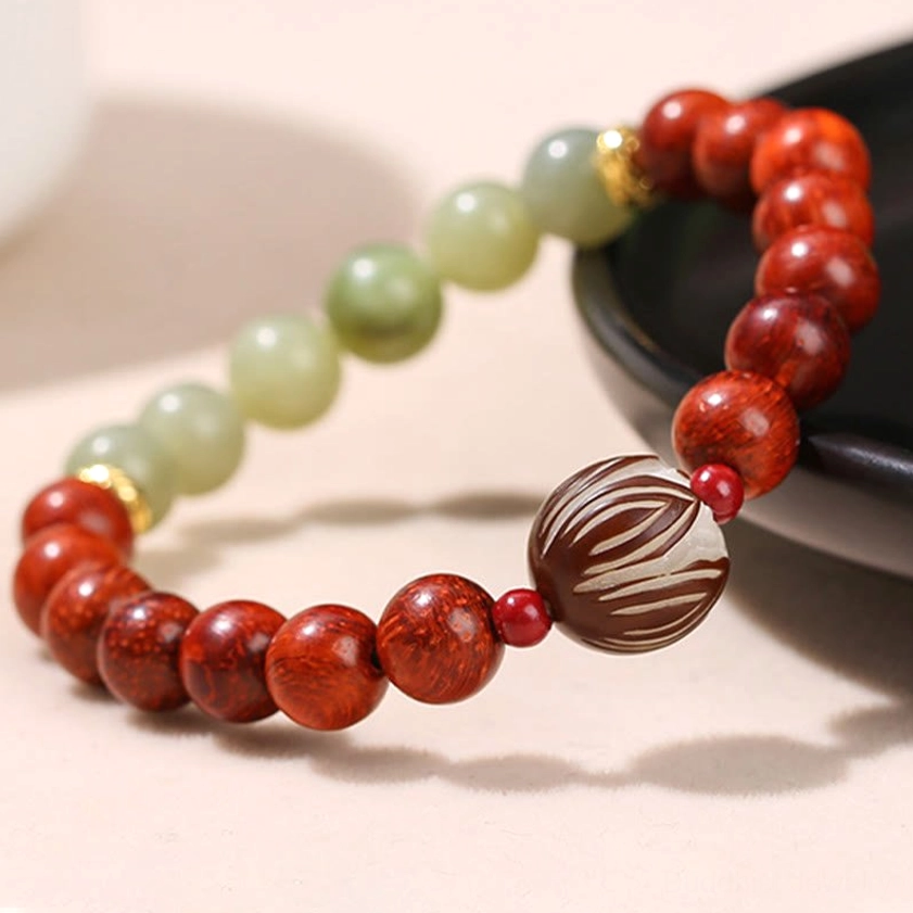 Side angle of Buddhist prayer bracelet showing natural wood grain and jade stone detail with red accent beads on black plate