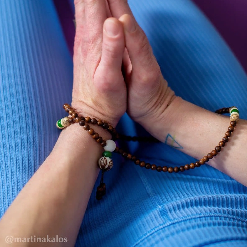 Wrist mala bracelet worn in yoga prayer gesture showing close-up of brown wooden beads and spiritual practice application
