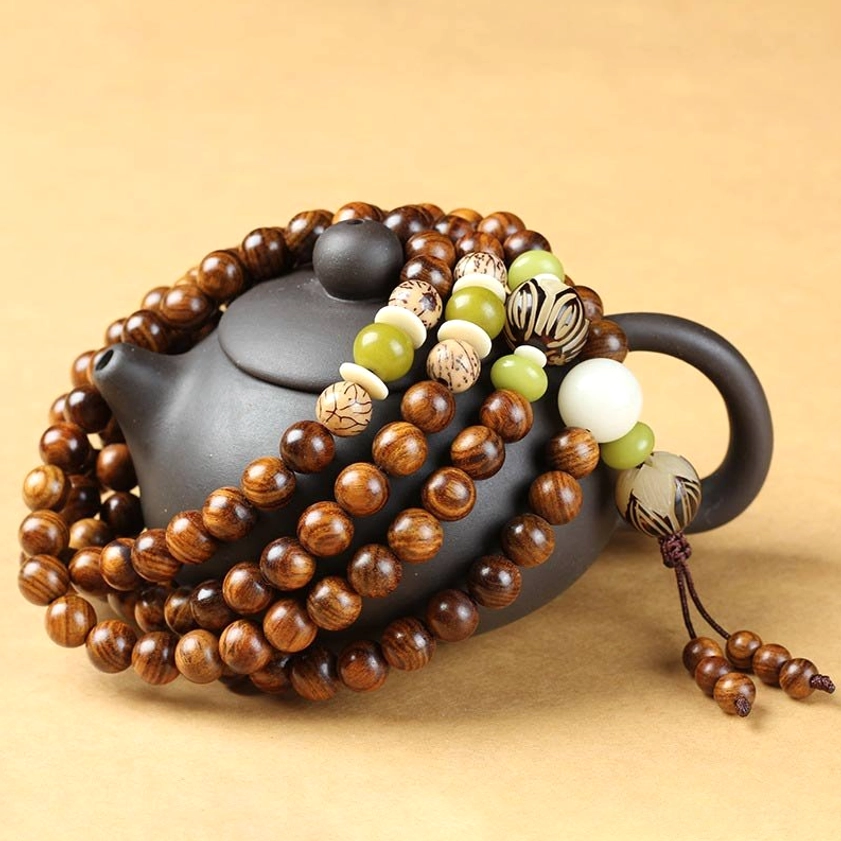 Rosewood mala bracelet wrapped around black teapot showing natural brown wood grain and decorative accent beads with tassel