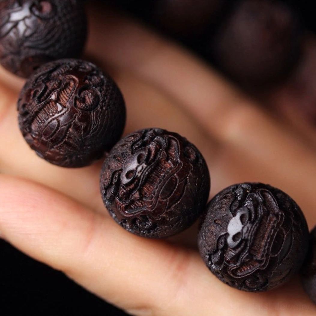 Single rosewood bead close-up with deep carved Pixiu patterns held between fingers
