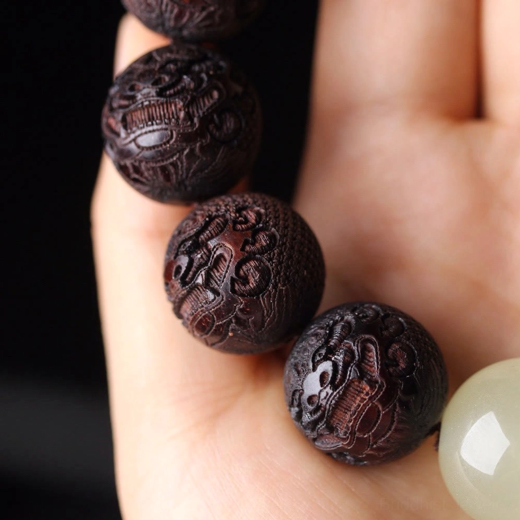 Partial rosewood Pixiu bracelet close-up showing hand-held carved beads with luminous spacer
