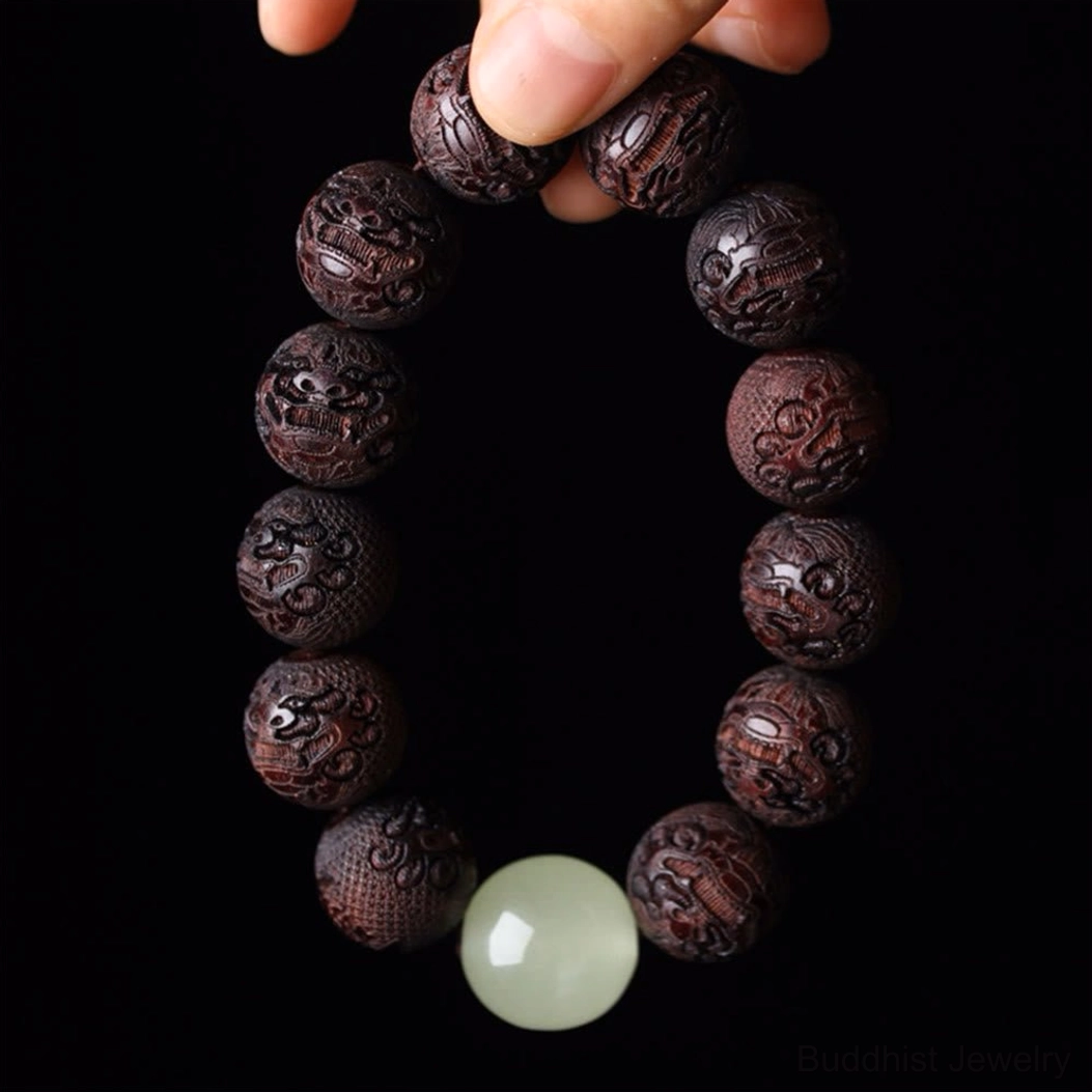 Rosewood Pixiu engraved Buddhist bracelet overhead view on black background with intricate carved beads and luminous spacer