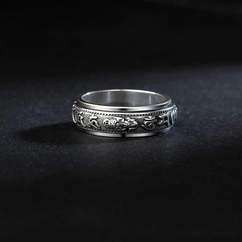 Top-down close-up of rotatable engraved buddhist ring showing beaded rim and embossed mantra patterns with vintage silver tone
