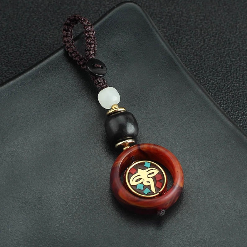 Overhead view of ebony wood Buddhist keychain with rotating golden emblem on black leather mat, dark brown and white color scheme