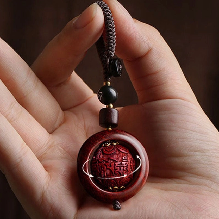 Red sandalwood rotating prayer keychain held at finger-level showing rotatable carved sphere with rotation arrows marked