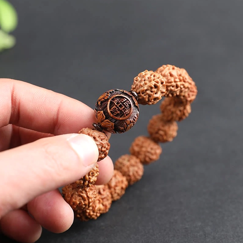 Close-up side view Rudraksha bracelet held by fingertips detailed carved wooden Pixiu accent bead