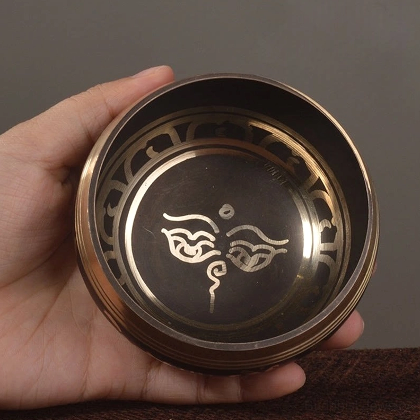 Handmade Buddhist singing bowl with Buddha eyes sacred script pattern held in hand, showing intricate gold engravings on black bronze surface