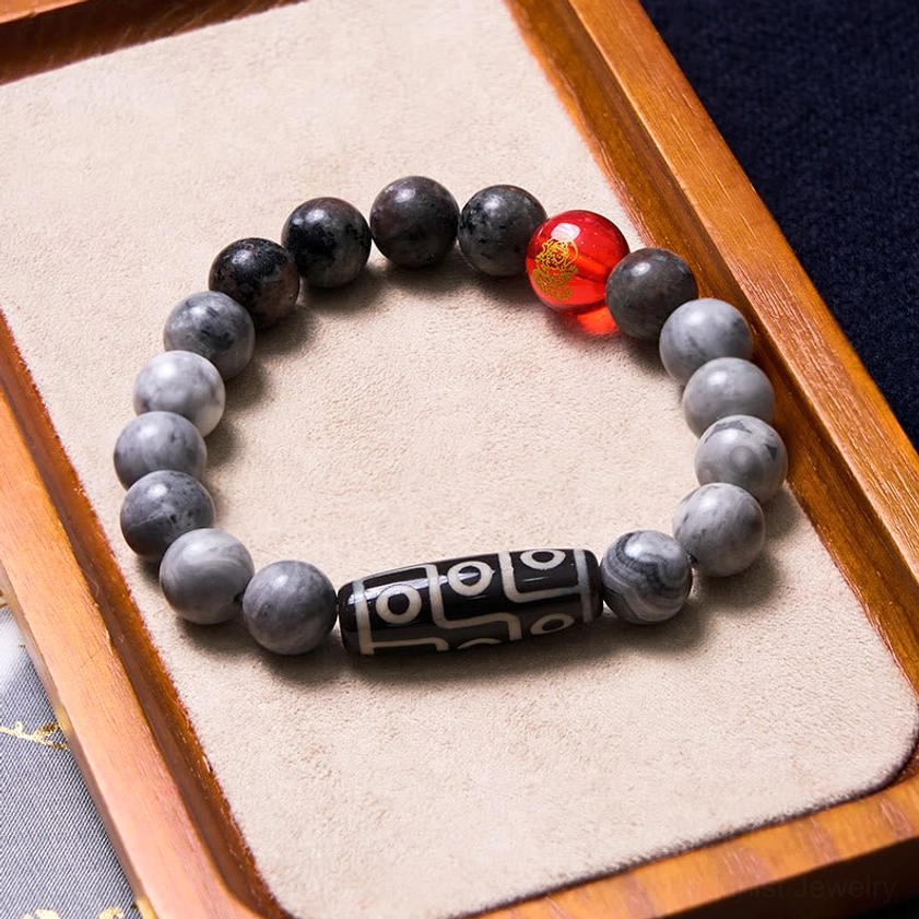 Buddhist bracelet with nine-eye dzi bead on wooden tray showing engraved red accent bead and matte stone composition