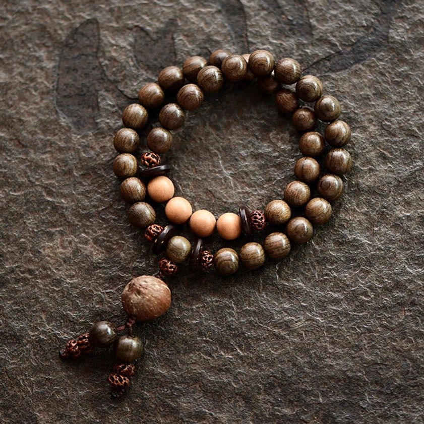 Double-loop sandalwood mala bracelet featuring uniform round wooden beads with protective tassel, flat lay view on textured brown fabric background